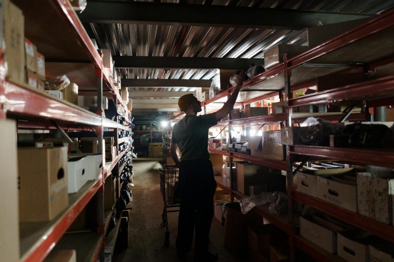 A worker arranging inventory on shelves in a dimly lit warehouse, utilizing efficient storage practices.